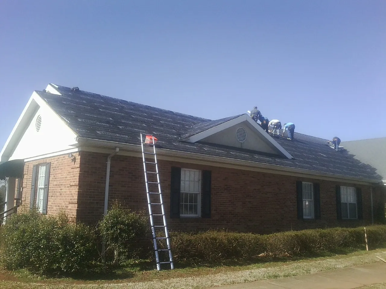 Crew tearing shingles off a brick ranch roof with a ladder set — Metal Roof Repair work by our crew in Maria Stein