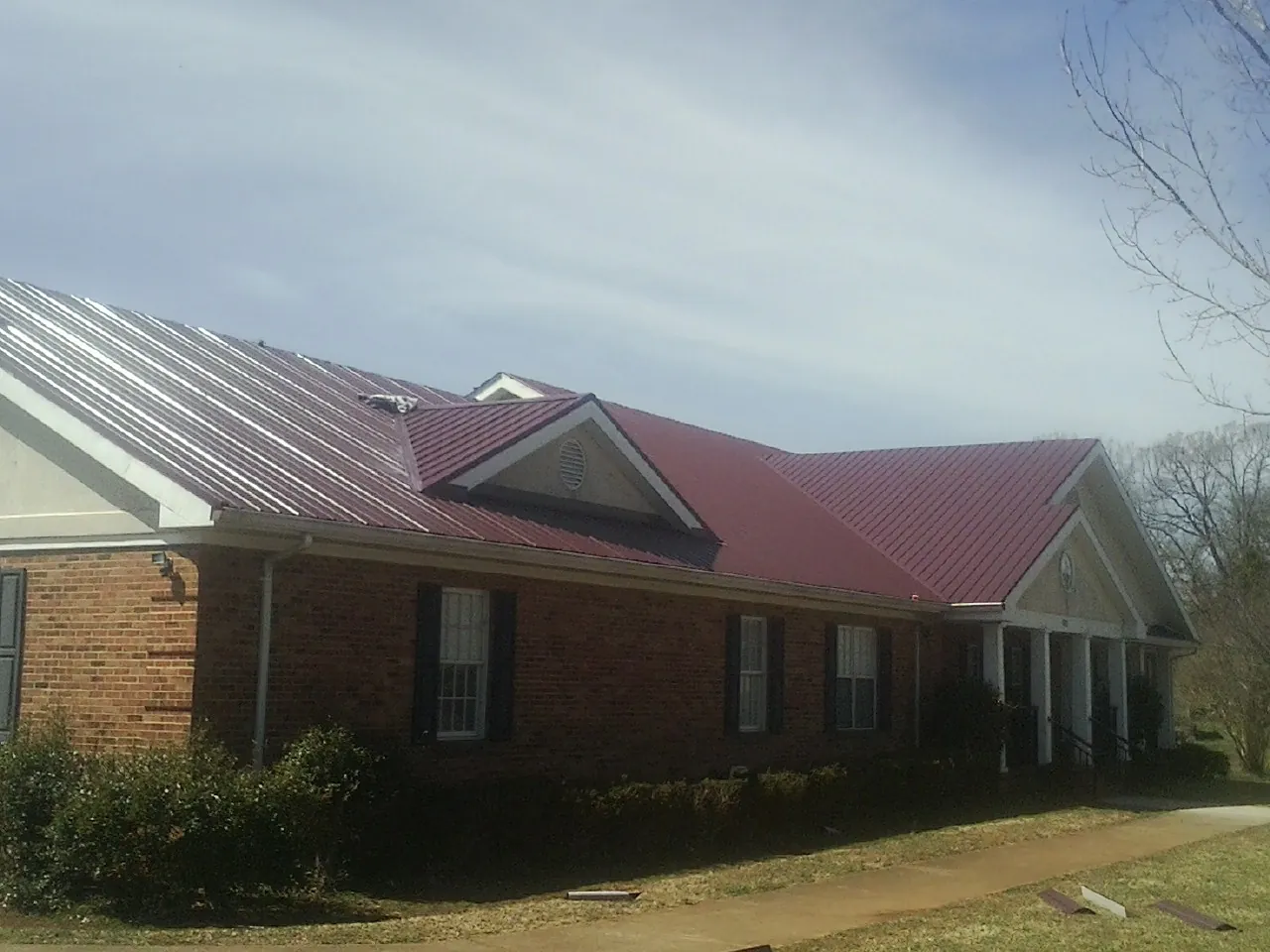 Red metal roof with gabled entries on a long brick building, from a Hail Damage Roof Repair job in Maria Stein