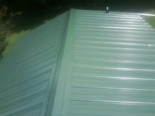 New green metal panels meeting at the ridge of a roof — Flat Roof Repair work by our crew in Maria Stein
