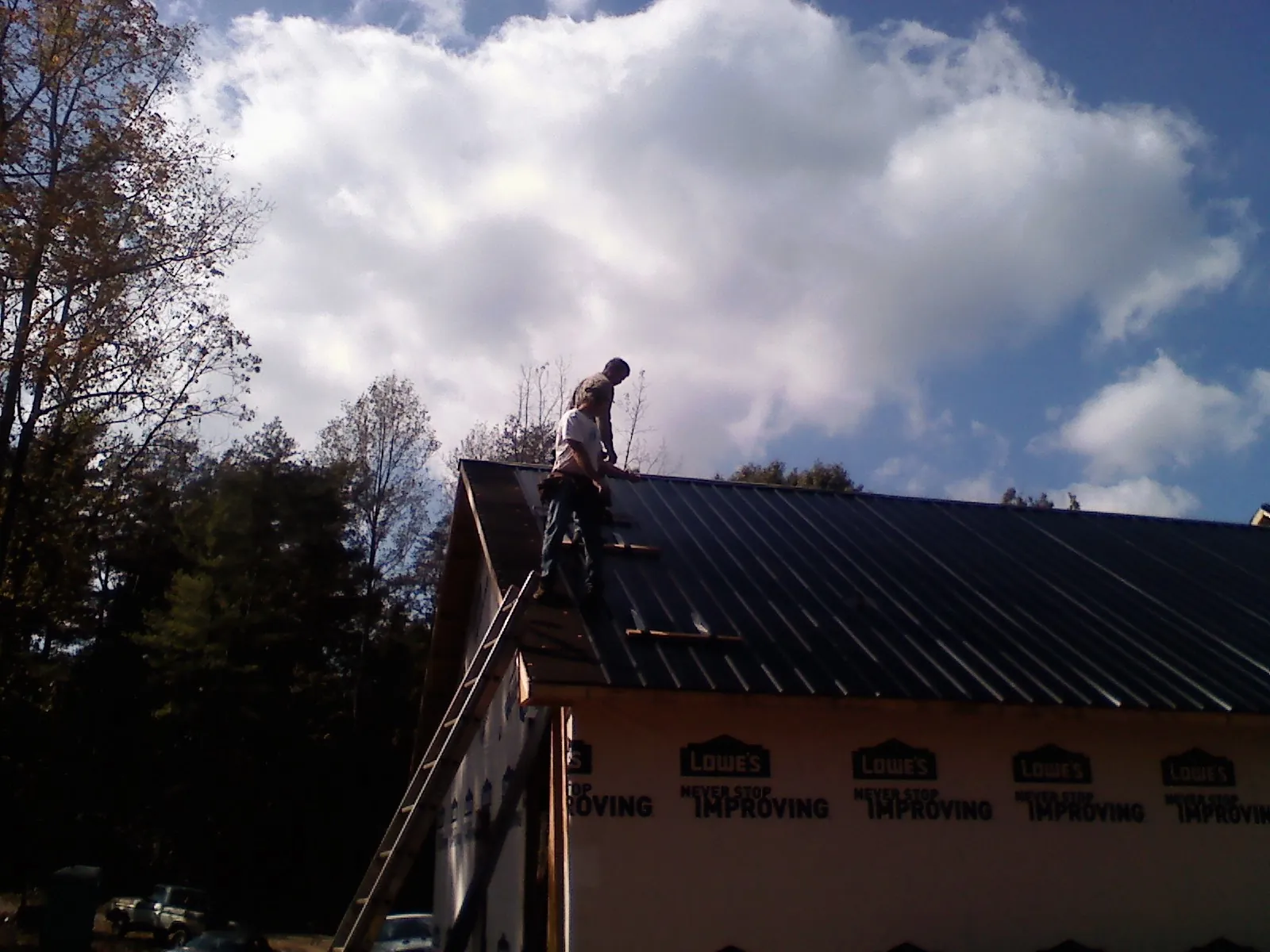 Roofer fastening dark metal panels high against a cloudy sky, from a Roof Inspection job in Maria Stein