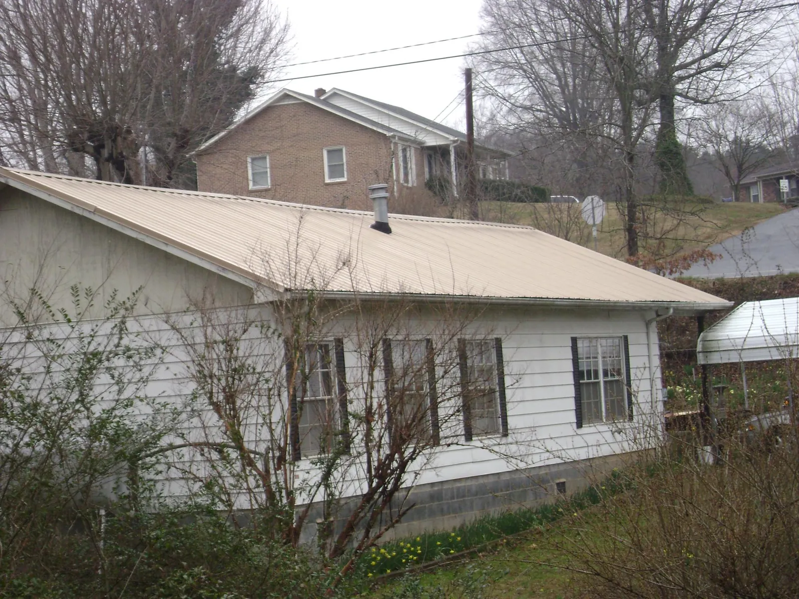 Tan metal roof on a white sided house set into a hillside — Commercial Roofing by Roofing Brothers in Maria Stein