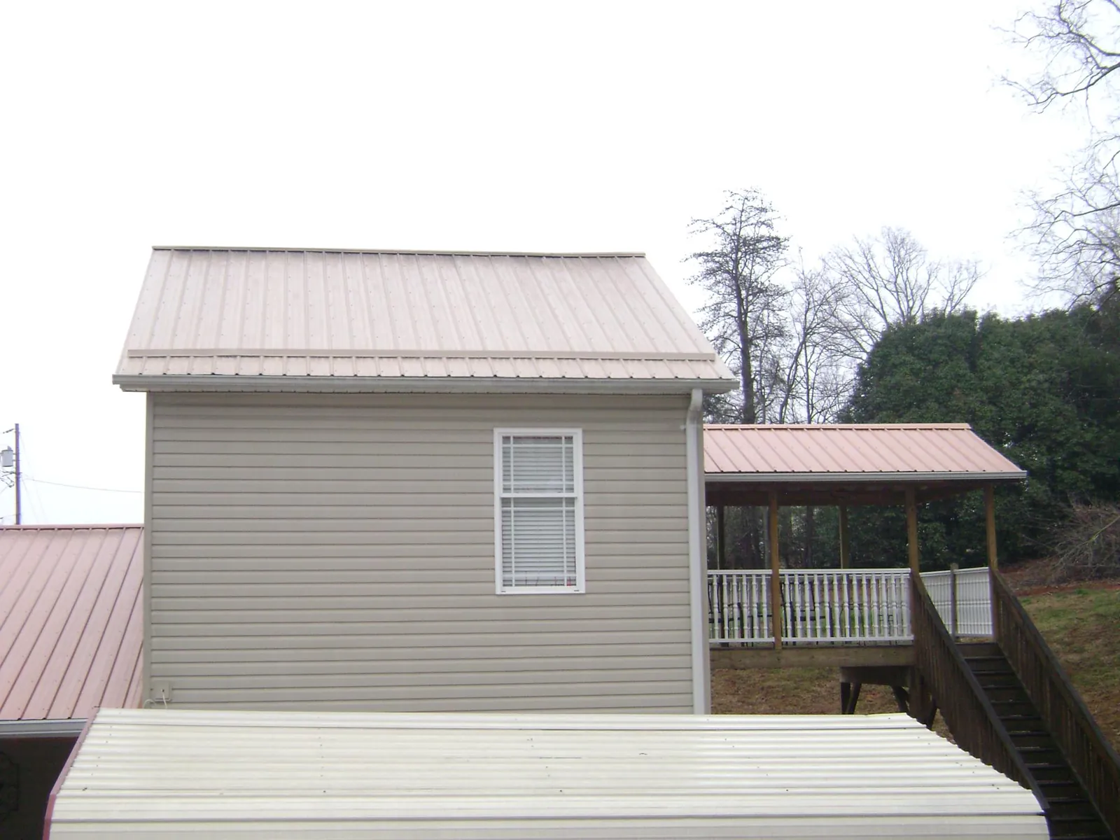 Tan metal roofs on a two story addition and attached porch, from a Roof Replacement job in Maria Stein